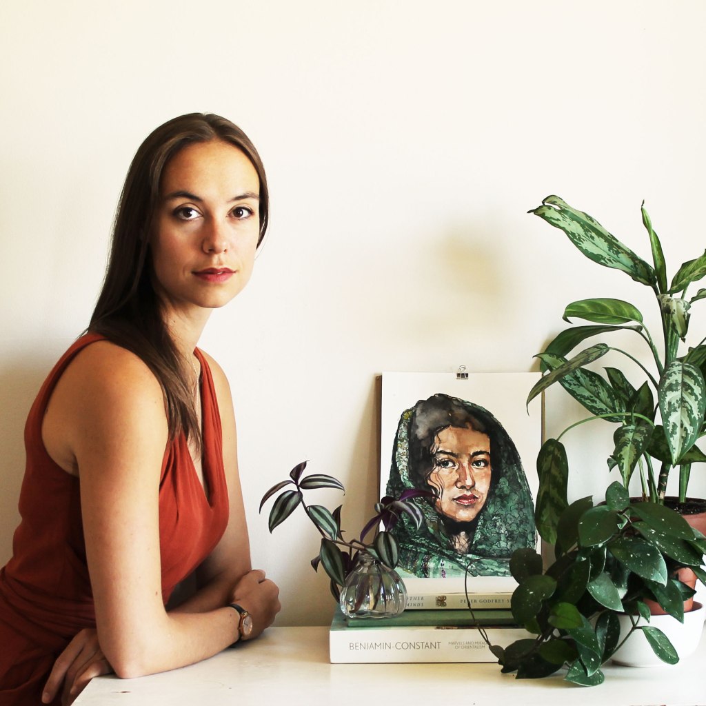 The artist with watercolour painting portrait of young woman in a green scarf, set among houseplants. Freelance illustration and custom portraits by Montreal Canadian artist.
